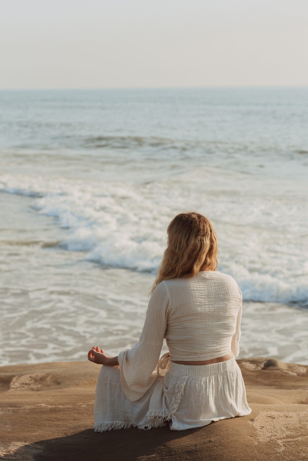 Malin sitzt meditierend am Strand mit Blick aufs Meer